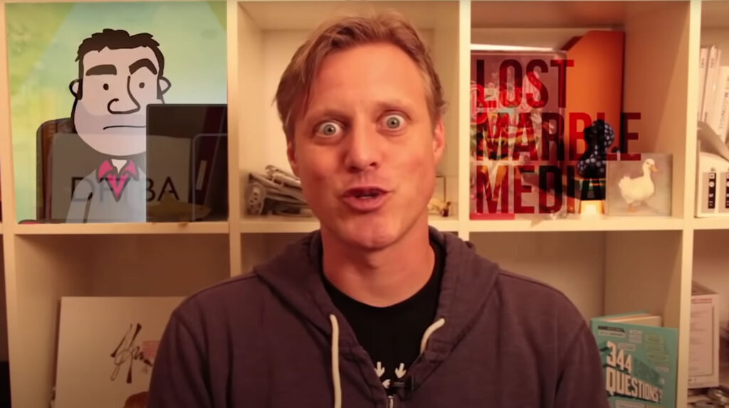 Ze Frank presenting 'a show' with a picture of Lee Hall and the Lost Marble logo on his shelves in the background.