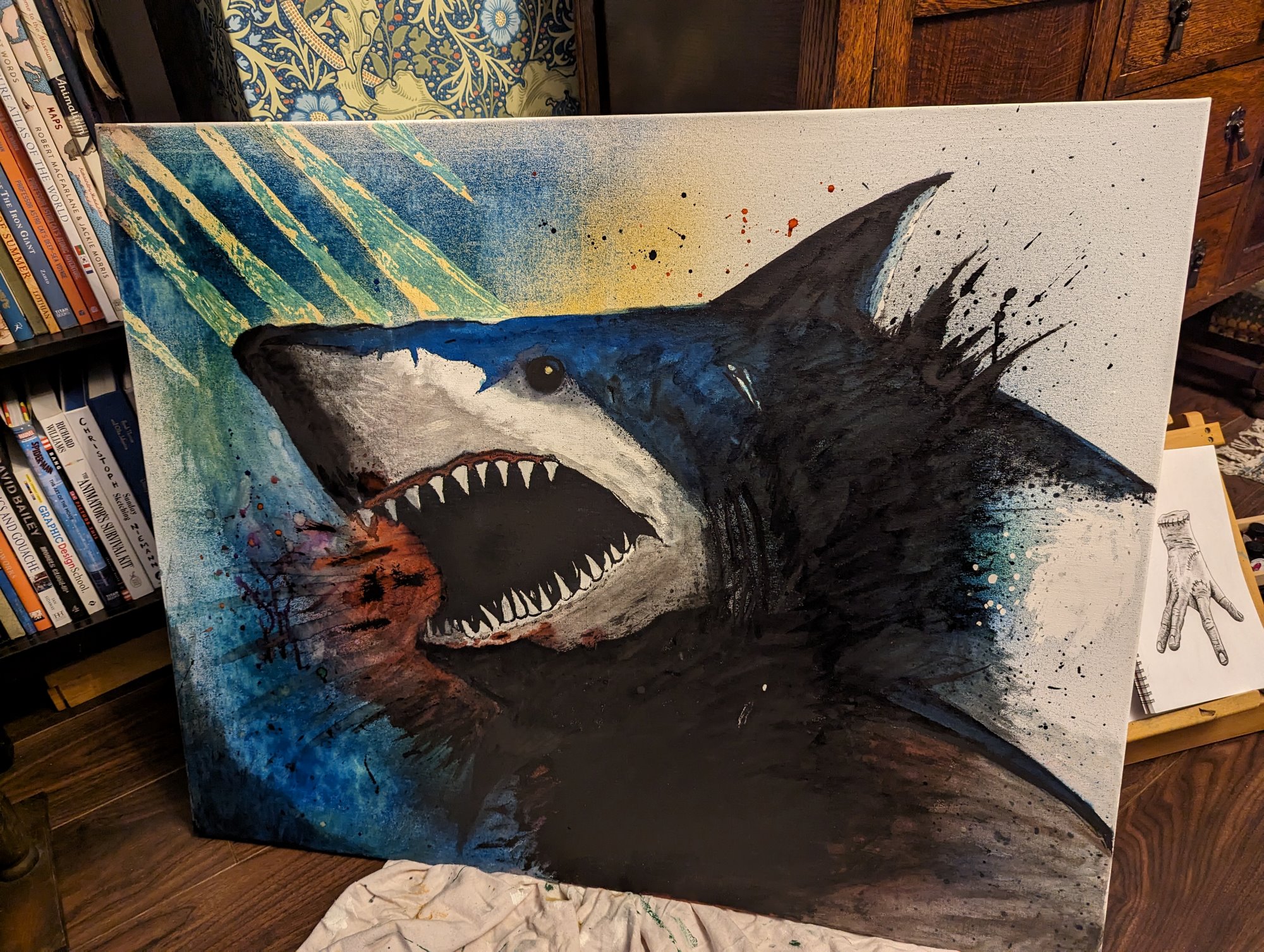 A shark painted with inks on a canvas with it's mouth open and spattered ink everywhere.